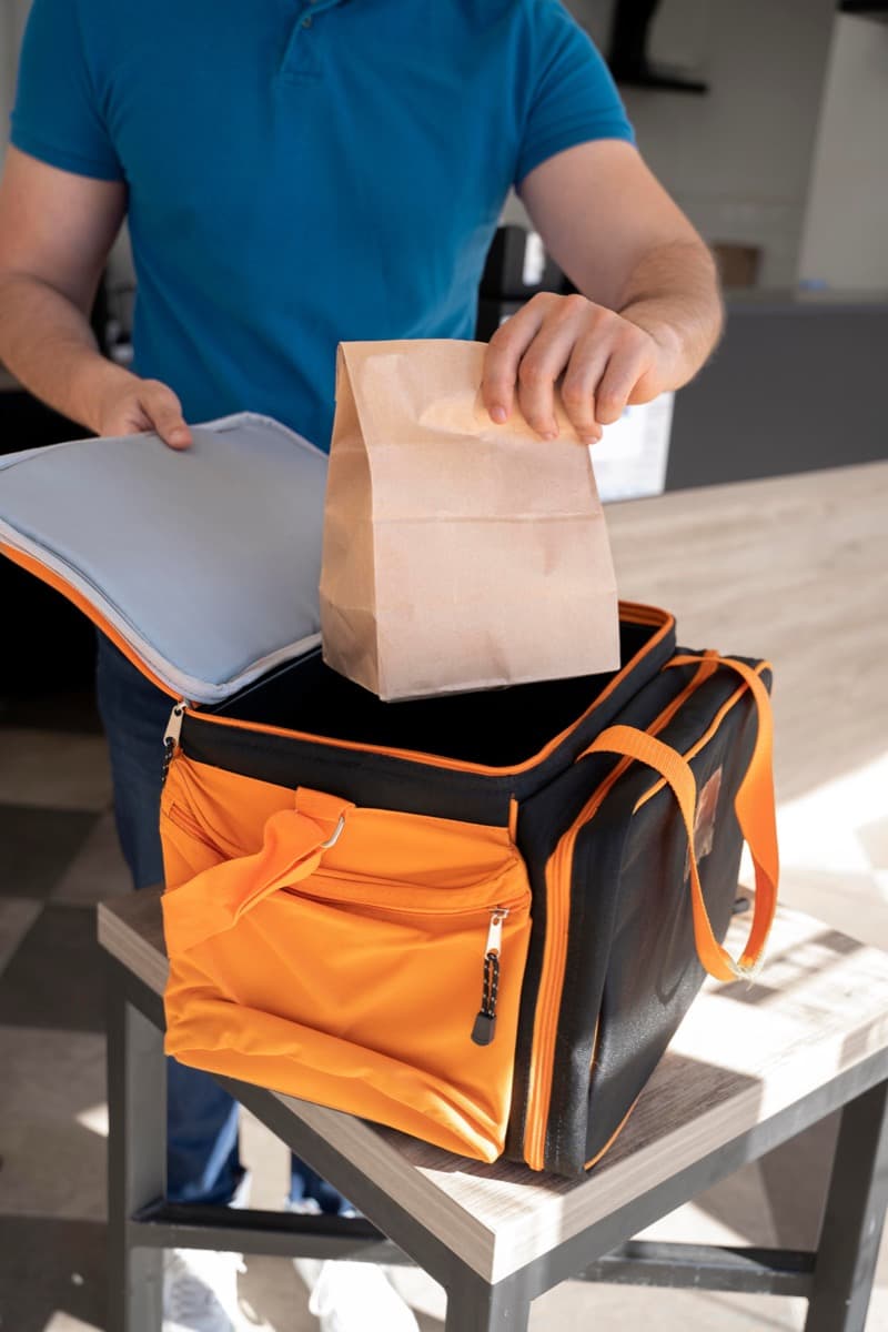Food delivery courier placing a meal order into a thermal bag