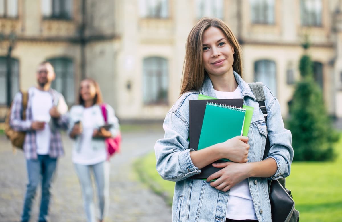 Student holding books on campus with peers in the background